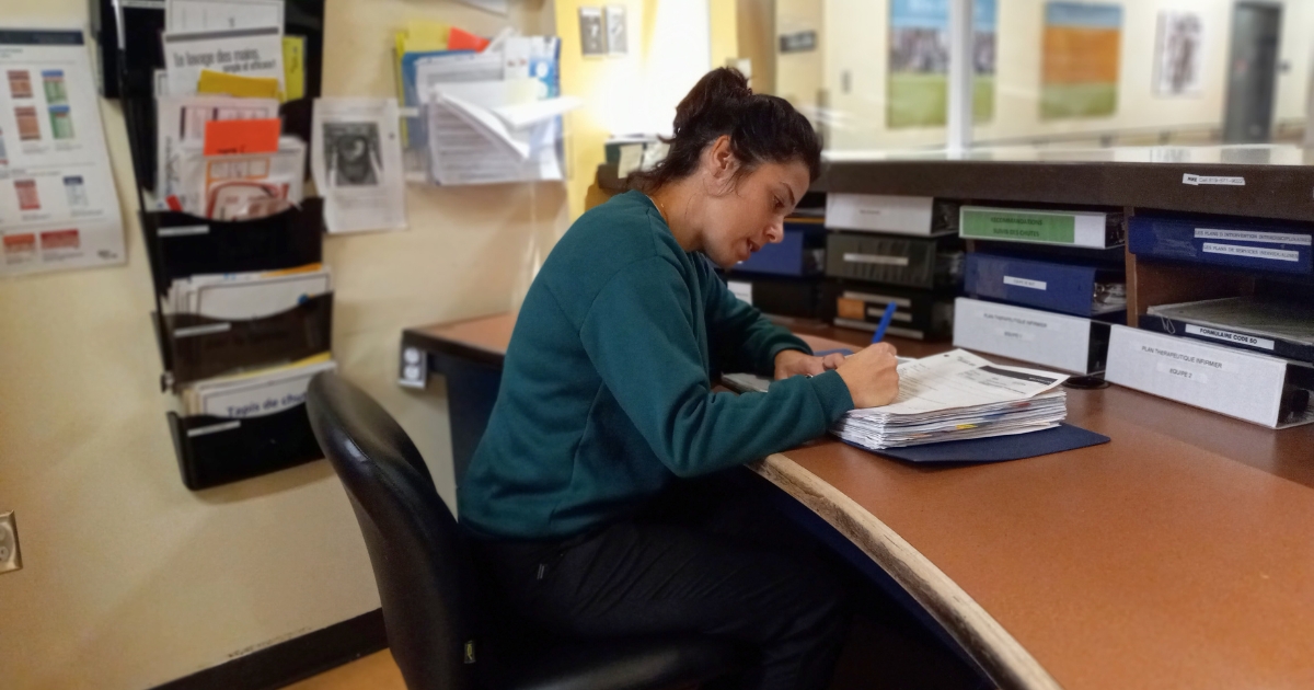 Conseillère-PCI-CIUSSS-Estrie Une femme aux cheveux bruns écrit dans un rapport assise à un bureau.