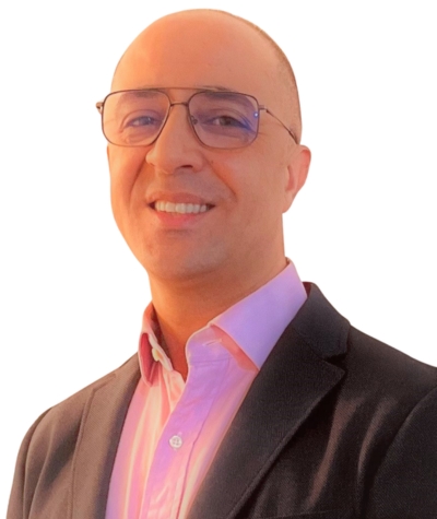 Hamid Remahi Un homme chauve à lunette portant un veston noir et une chemise rose.