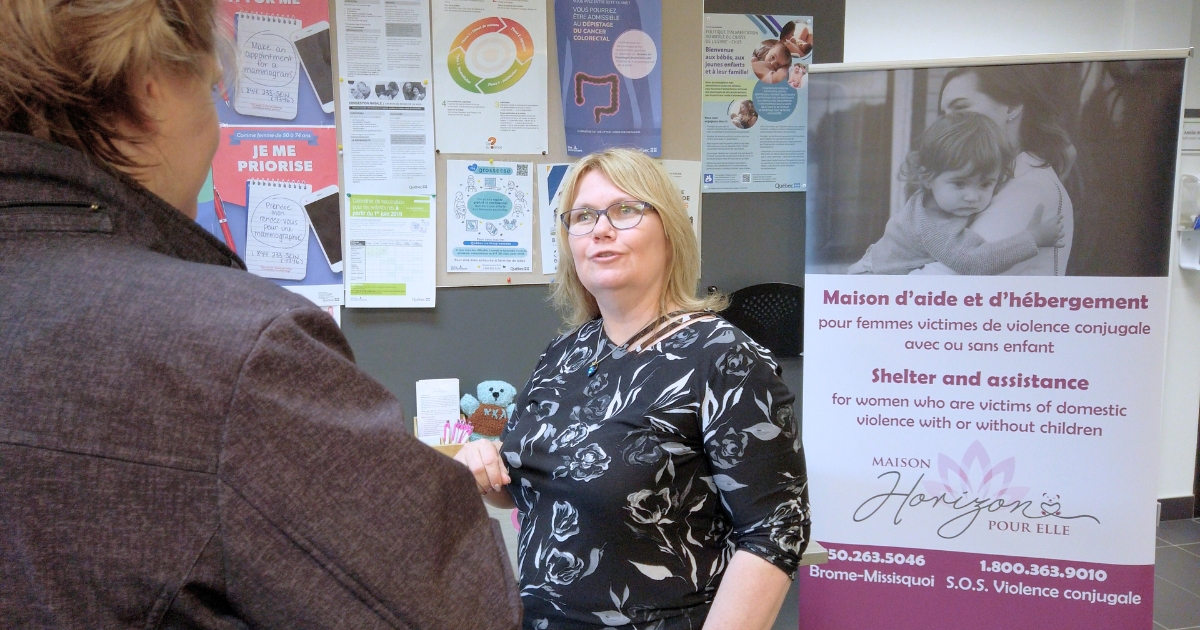 Deux femmes discutant devant une affiche promotionnelle intérieure.<br />
