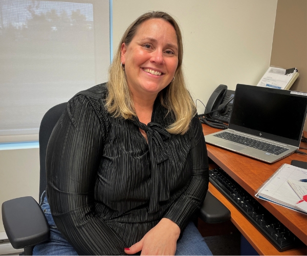 Une femme blonde souriante à son bureau. 
