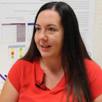 Une femme aux cheveux bruns et portant un chandail rouge.