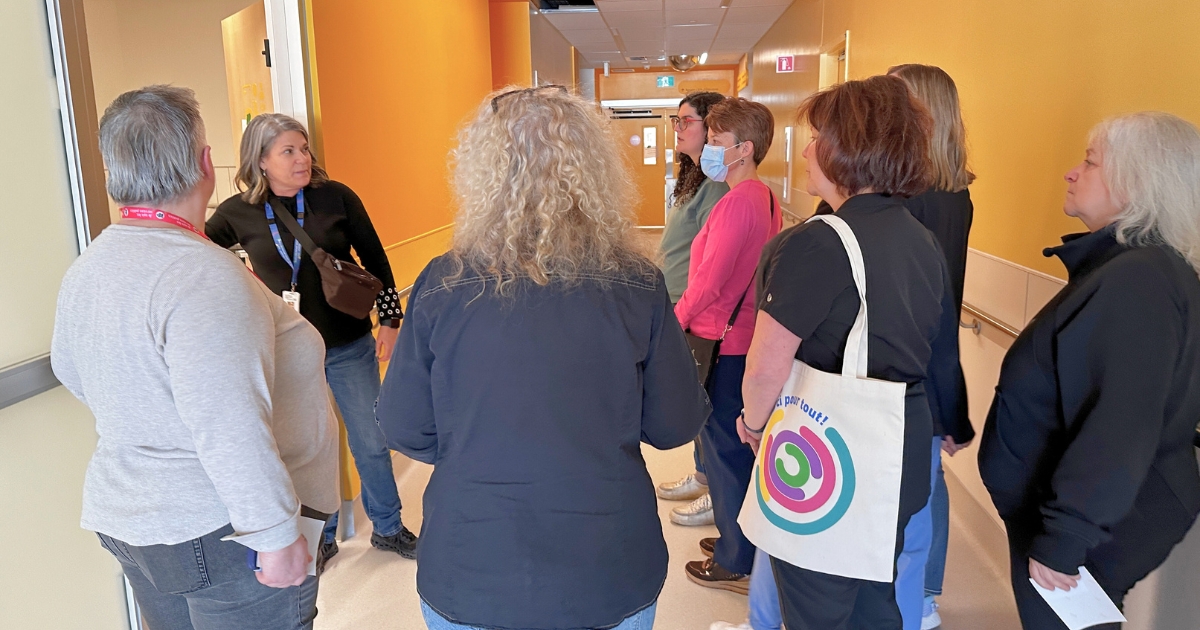 Une femme aux cheveux blancs présente les locaux jaune à un groupe. 