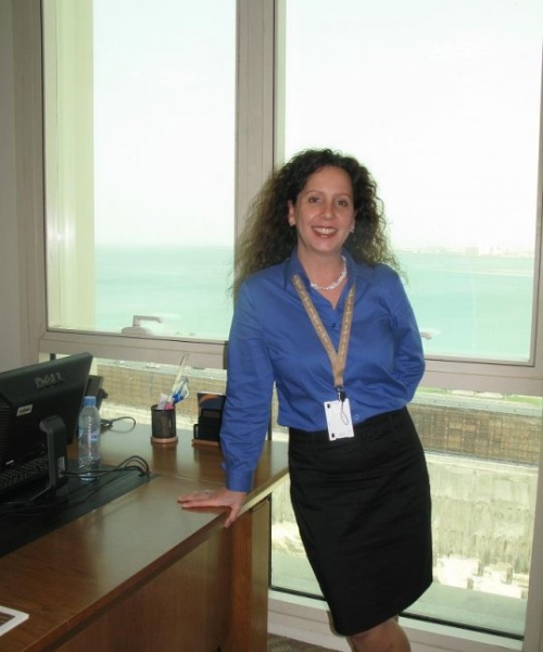 Une femme aux cheveux frisés posant fièrement dans une tour à bureaux vitrée. 