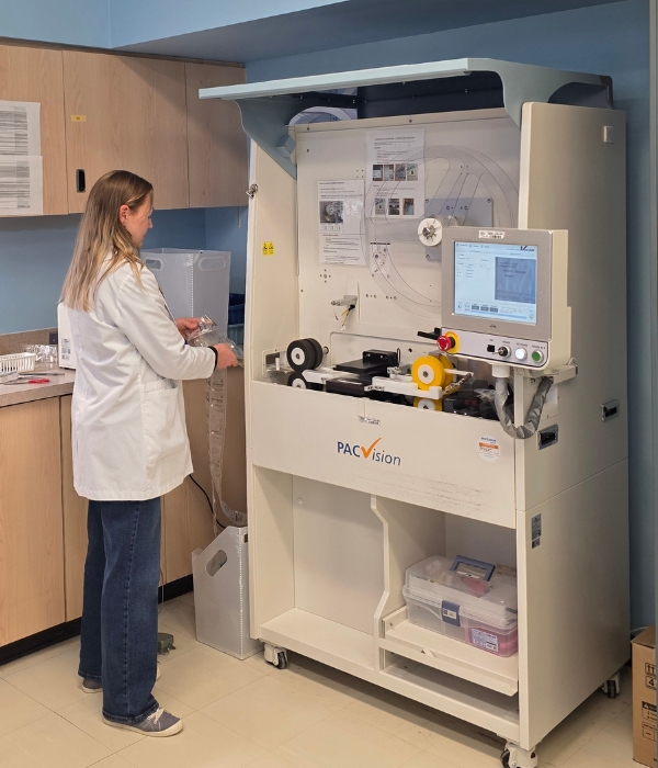 Une femme en sarrau debout devant une machine.