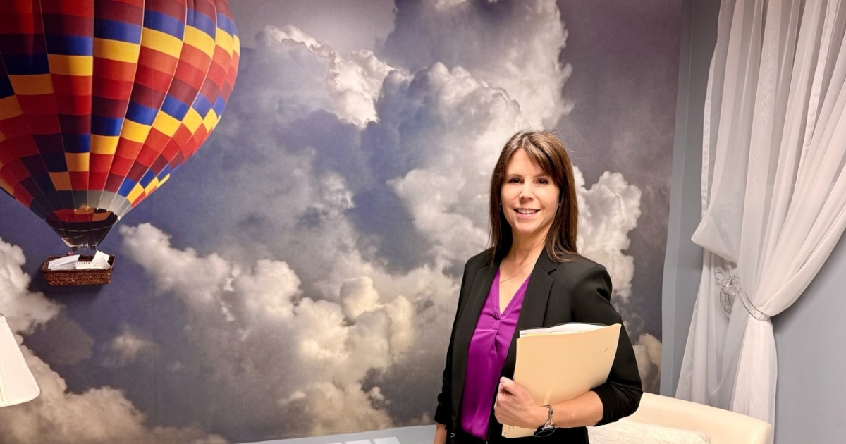 Une femme aux cheveux bruns devant une murale de montgolfière.